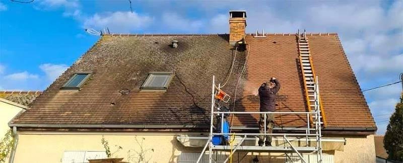 Nettoyage d’une toiture au jet depuis un échafaudage, la partie traitée apparaît nettement plus claire