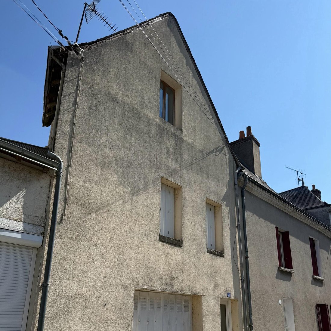 Pignon de maison de bourg avant ravalement, enduit taché et débord de toit dégradé